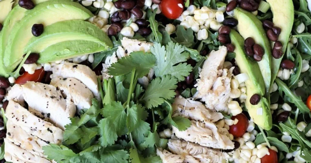 A Colorful Healthy southwestern salad with chicken, featuring cooked chicken, mixed greens, black beans, corn, tomatoes, avocado, and a tangy dressing