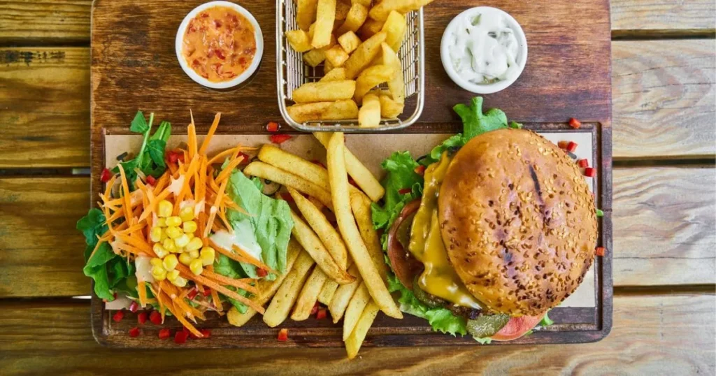 Step by step guide to crafting the ultimate bison hamburger, featuring fresh lettuce, ripe tomatoes, onion, and pickles, served with crispy French fries, a refreshing salad, and two delicious dipping sauces